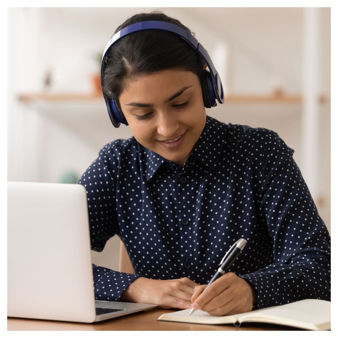 Girl writing in a notebook sitting in front of a laptop