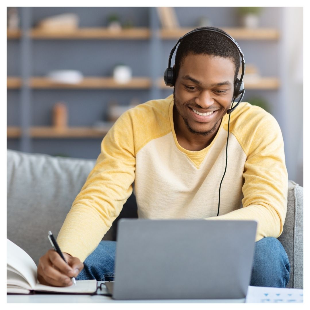 Man taking an online class, taking notes and smiling